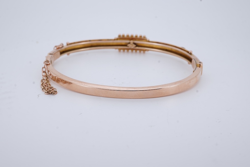 An Edwardian 9ct, seed pearl and ruby set hinged bangle, interior diameter 57mm, gross weight 8.3 grams. Condition - poor to fair